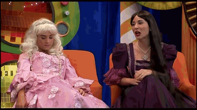 a man in a pink dress sits next to a woman in a purple dress .
