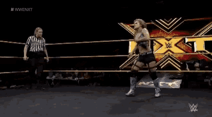 a woman is jumping in a wrestling ring while a referee looks on .