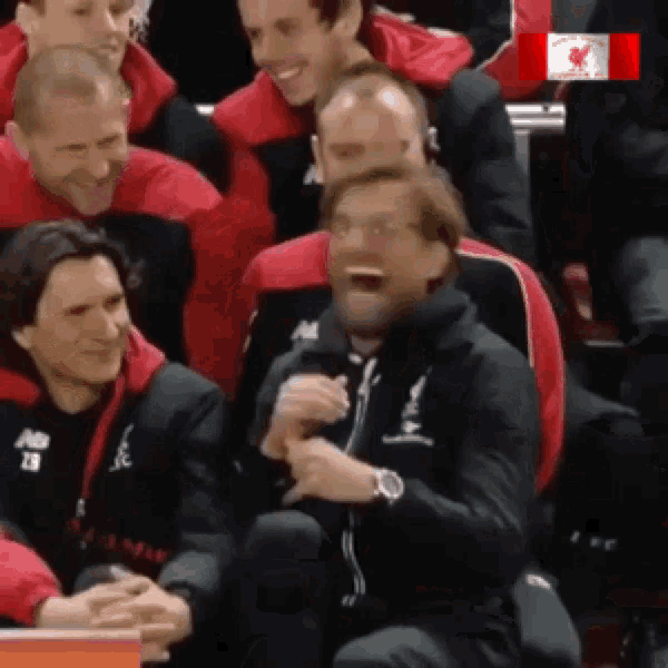a group of soccer players are sitting in a stadium and one of them is wearing a black jacket that says liverpool