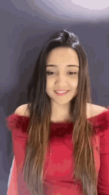a woman is wearing a red off the shoulder top and smiling .