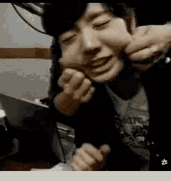 a person is making a funny face with their hands while sitting in front of a laptop .