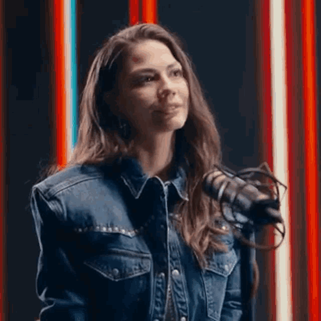 the woman is wearing a denim jacket and standing in front of a microphone .