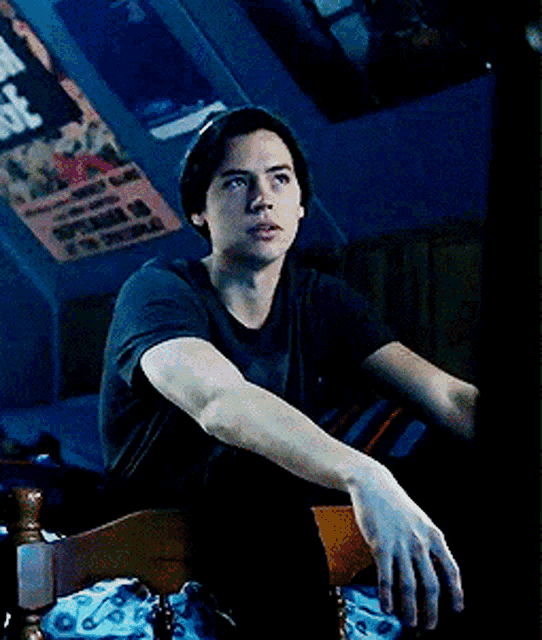 a young man sitting on a bed with posters on the wall including one that says ' i 'm sorry '
