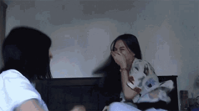 two women are sitting on a bed laughing and covering their mouths