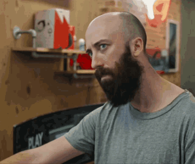 a bald man with a beard is looking at something in front of a play sign