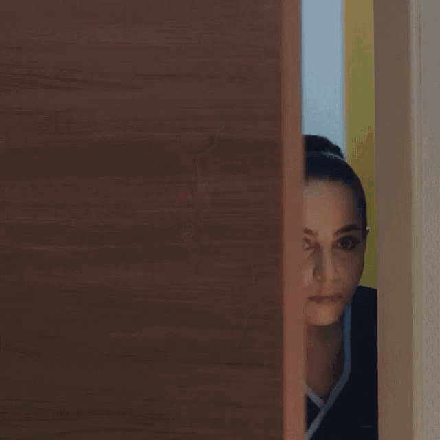 a woman in a black scrub top is peeking out of a doorway .