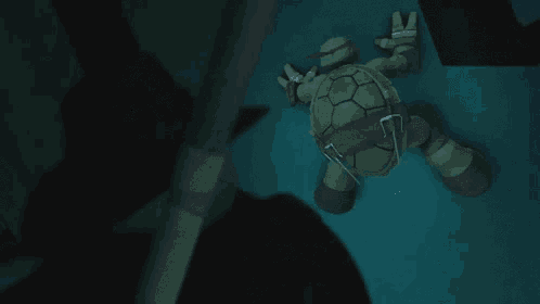 a teenage mutant ninja turtle is laying on the floor and giving the peace sign .