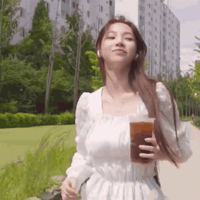 a woman in a white dress is holding a cup of coffee while walking down a sidewalk .