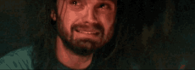 a man with long hair and a beard is looking at the camera with a red light shining on his face .