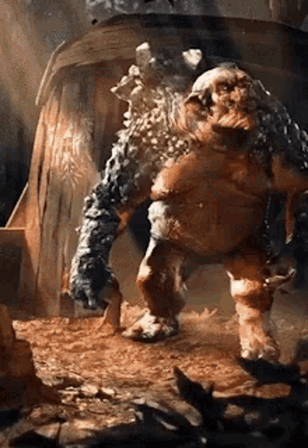 a large monster is standing on a pile of dirt in front of a wooden structure .