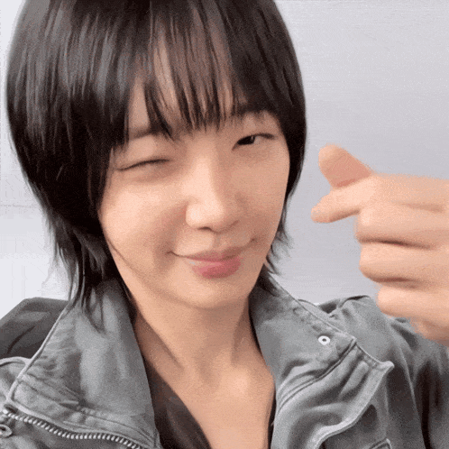 a woman with short black hair is making a heart with her fingers