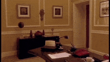 a room with a desk , chair , lamp and a red phone .