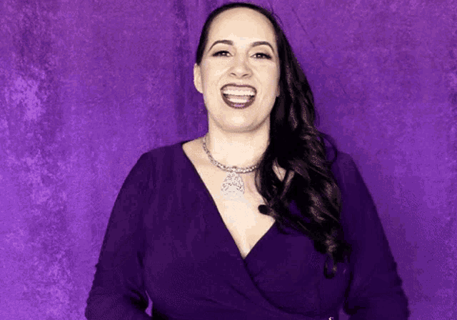 a woman wearing a purple dress and a necklace is laughing .