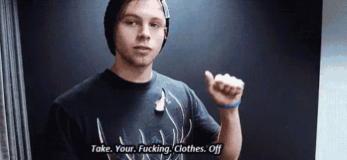 a young man wearing a beanie and a t-shirt is standing in front of a black wall and talking .