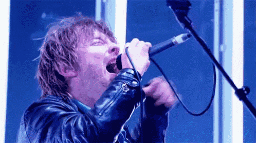 a man in a leather jacket is singing into a microphone on a stage .