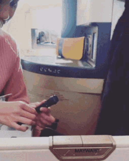 a woman sitting on an airplane looking at her phone with the word maywand visible