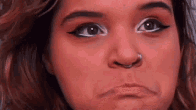 a close up of a woman 's face with a nose ring making a sad face .
