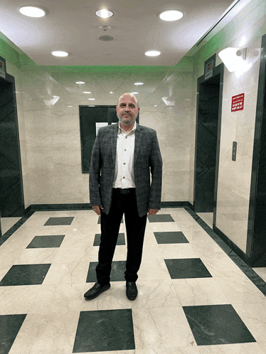 a man in a suit stands in a hallway with elevators and a sign that says " no smoking "