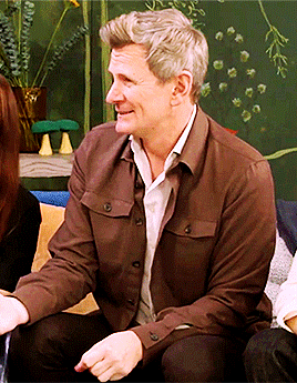 a man in a brown jacket sits on a couch with a woman