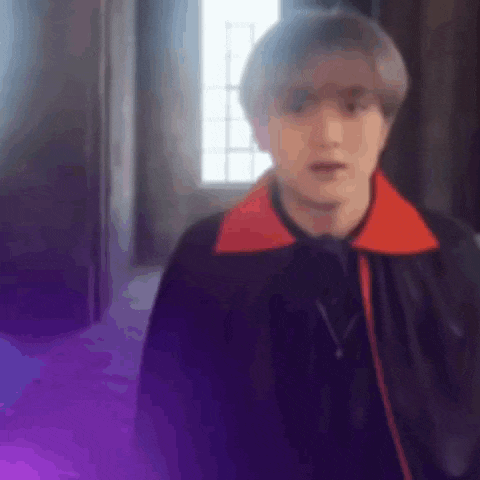 a man in a black jacket and red collar is standing in a room with purple smoke coming out of the window .