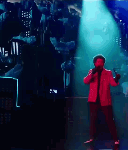 a man in a red jacket is singing into a microphone on stage