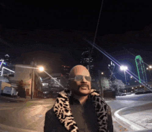 a man wearing sunglasses and a leopard print jacket is standing on a city street at night