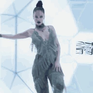 a woman in a green dress is dancing in front of a white wall .
