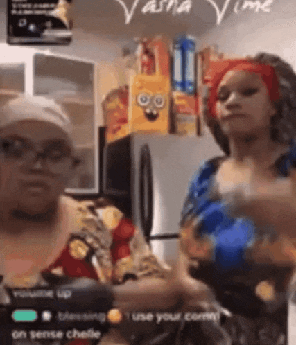 two women are dancing in a kitchen with a spongebob bag on the wall behind them