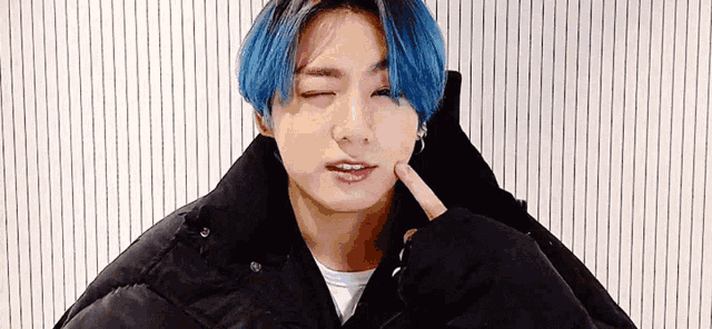 a young man with blue hair and a black jacket is making a funny face .