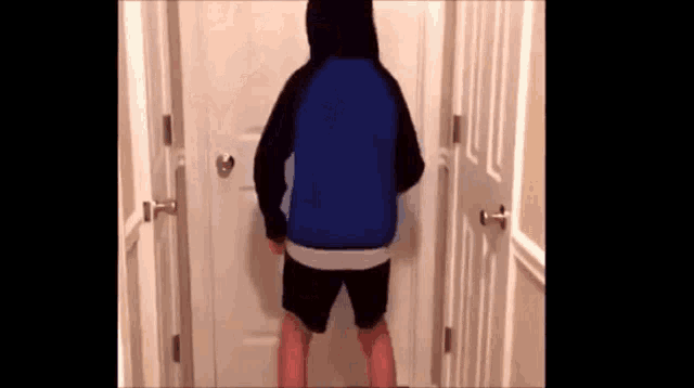 a man in a blue hoodie and black shorts is standing in front of a door .