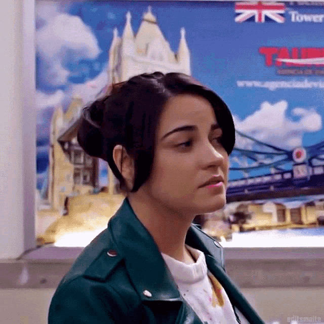 a woman in a green leather jacket is standing in front of a poster that says tower bridge