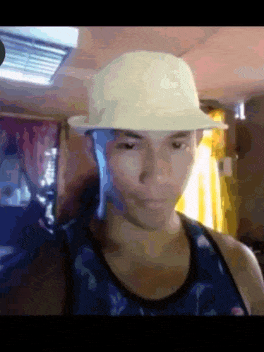 a young man wearing a hat and a tank top looks at the camera