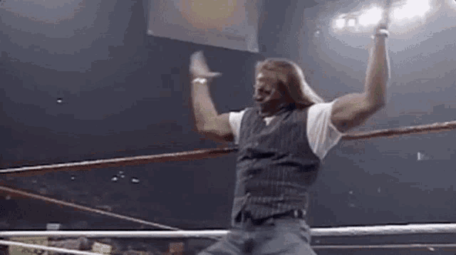 a man is standing in a wrestling ring with his hands in the air .