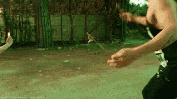 a man without a shirt is fighting another man with a stick in a park .
