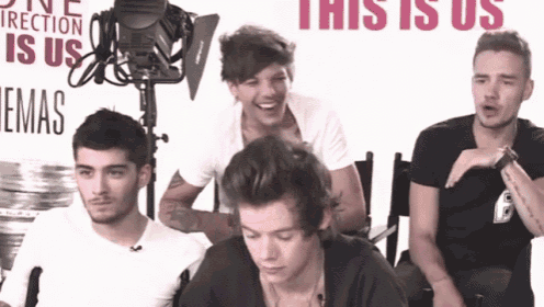 a group of young men sit in front of a sign that says one direction is us