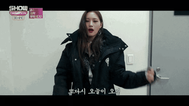 a woman in a black jacket is standing in front of a door with show champion behind written on the bottom
