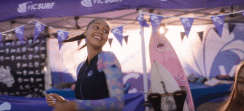 a woman in a wetsuit is standing in front of a purple tent that says picsurf