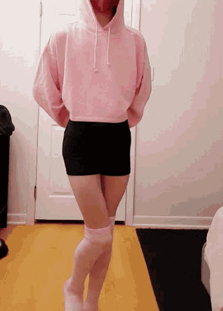 a woman in a pink hoodie and pink knee high socks stands in front of a door