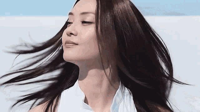 a woman 's hair is blowing in the wind and she is wearing a white shirt
