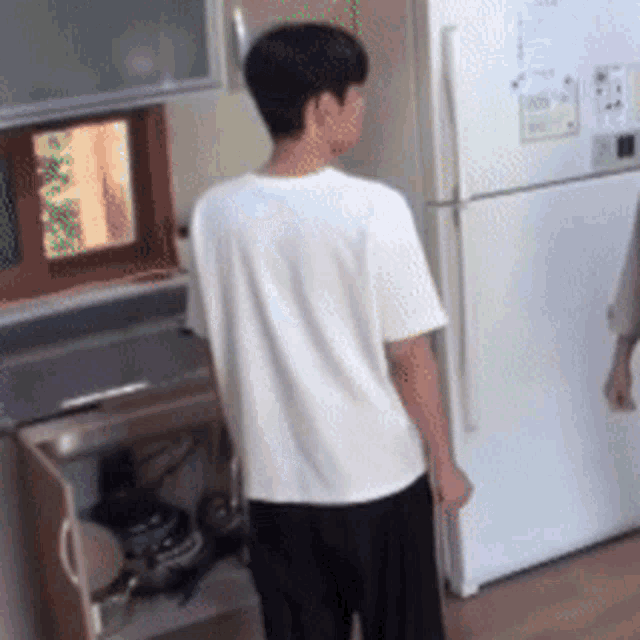a man in a white shirt is standing in a kitchen next to a refrigerator
