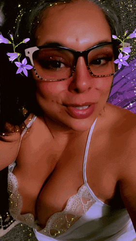 a woman wearing glasses and a white tank top takes a selfie