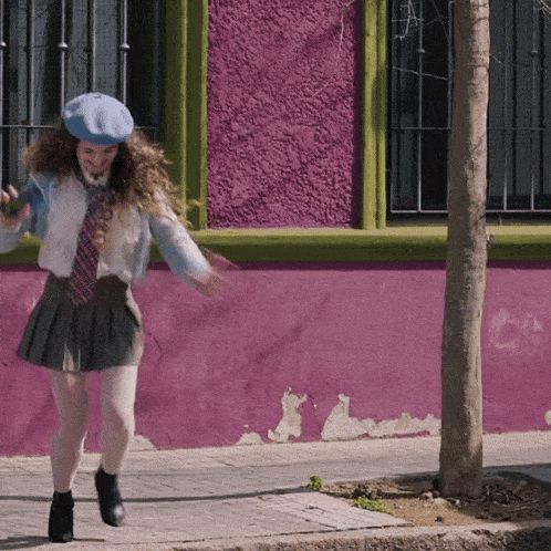 a girl wearing a beret and a skirt is dancing in front of a pink wall