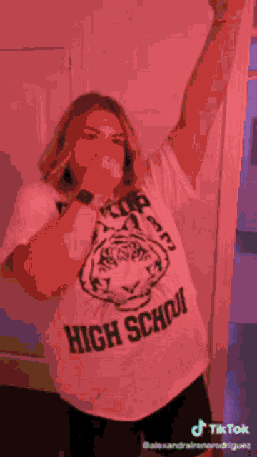 a woman wearing a high school shirt is covering her mouth