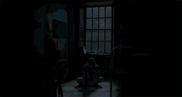 a woman with long blonde hair and bangs is sitting in a dark room looking at the camera .