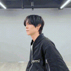 a man in a black jacket is standing in a room with the word jemi written on it .