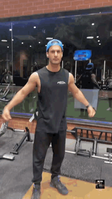 a man wearing a black tank top and a blue hat is in a gym