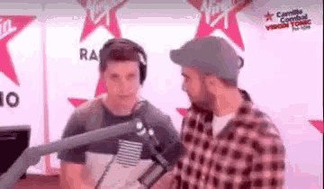 two men are talking to each other in front of a microphone in a radio studio .