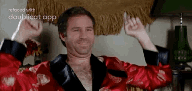a man in a red robe is sitting in a chair with his arms in the air .