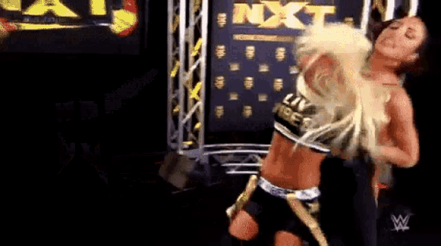 two women are wrestling on a stage in front of a sign that says nxt .