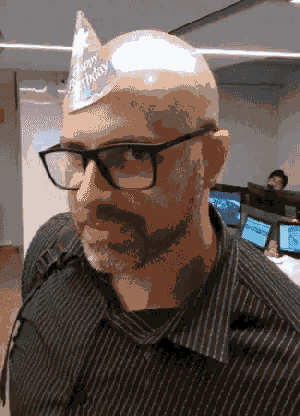 a bald man wearing glasses and a birthday hat